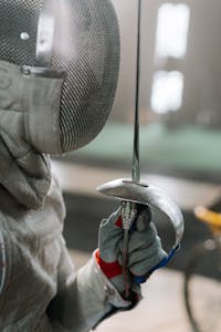 Focused shot of a fencer holding a foil during a match, showcasing sports gear details.